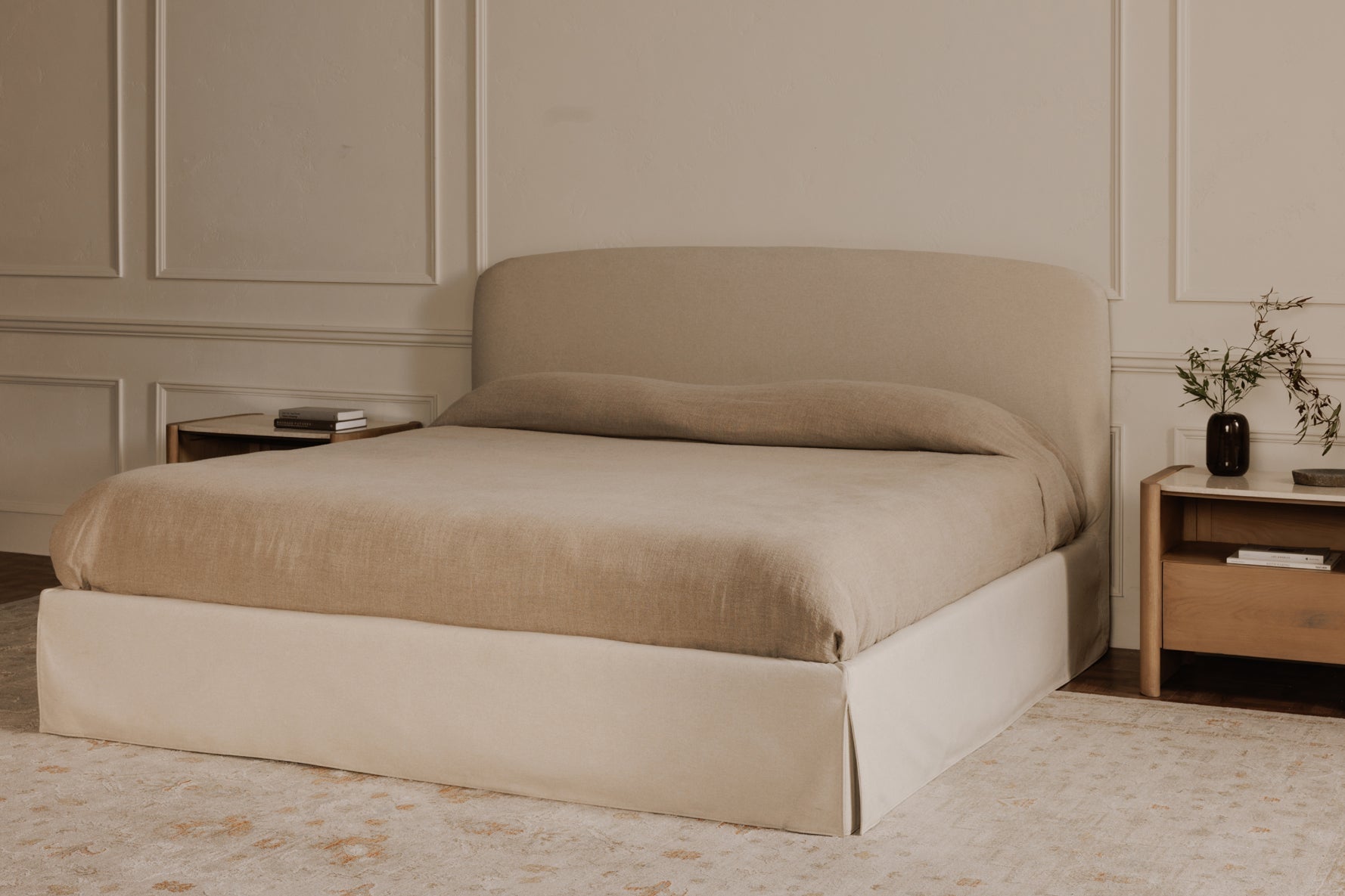 Beige bed in a bedroom with wooden nightstands and decorative items.