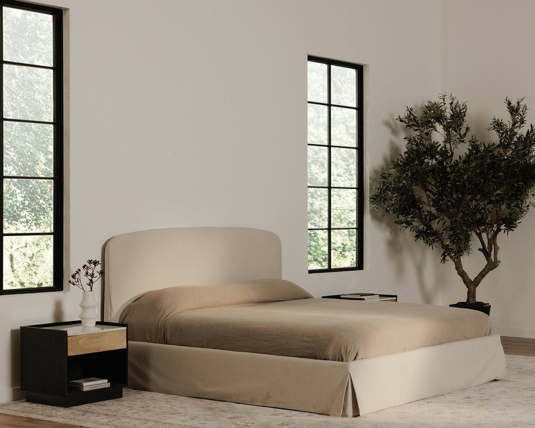Beige bed in a room with large windows and a plant