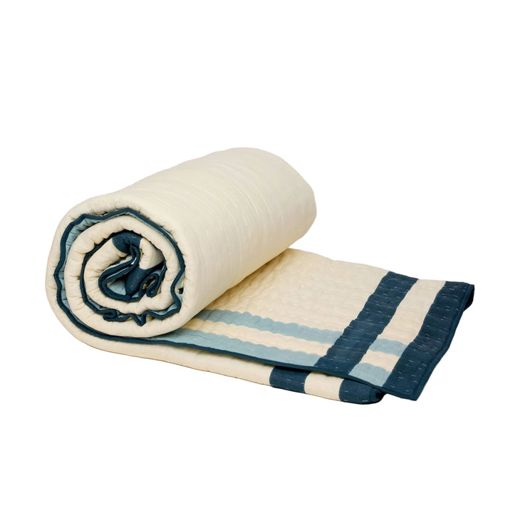 Rolled-up quilt with blue and beige stripes on a light gray background