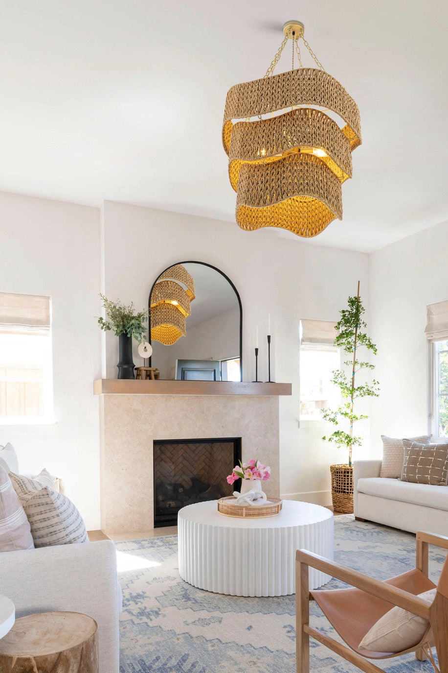 Modern living room with a wicker chandelier, white sofas, and a fireplace.