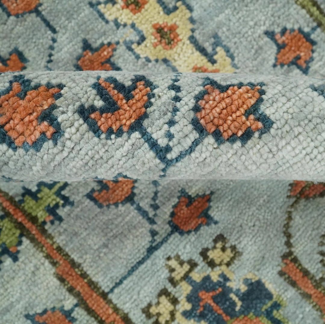 Close-up of a patterned rug with geometric designs in orange, blue, and green on a light gray background.