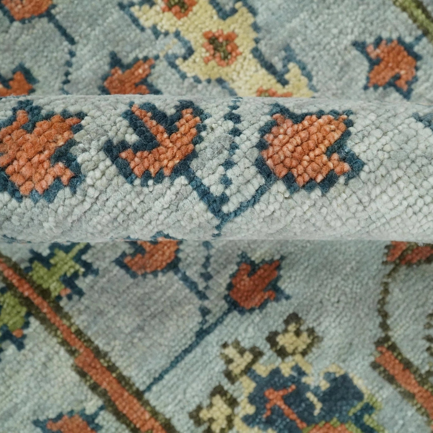 Close-up of a patterned rug with geometric designs in orange, blue, and green on a light gray background.